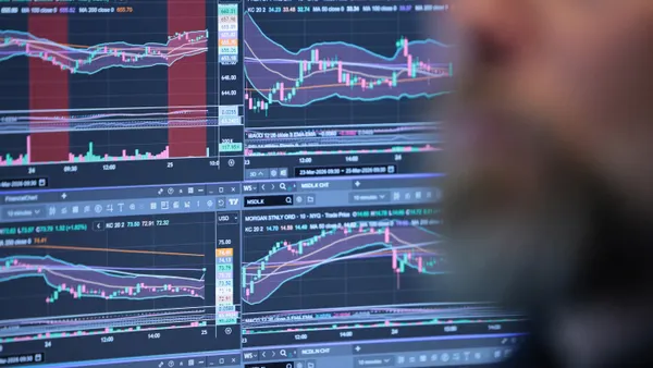 A person's head is seen in front of a computer showing a variety of line graphs with stock symbols.