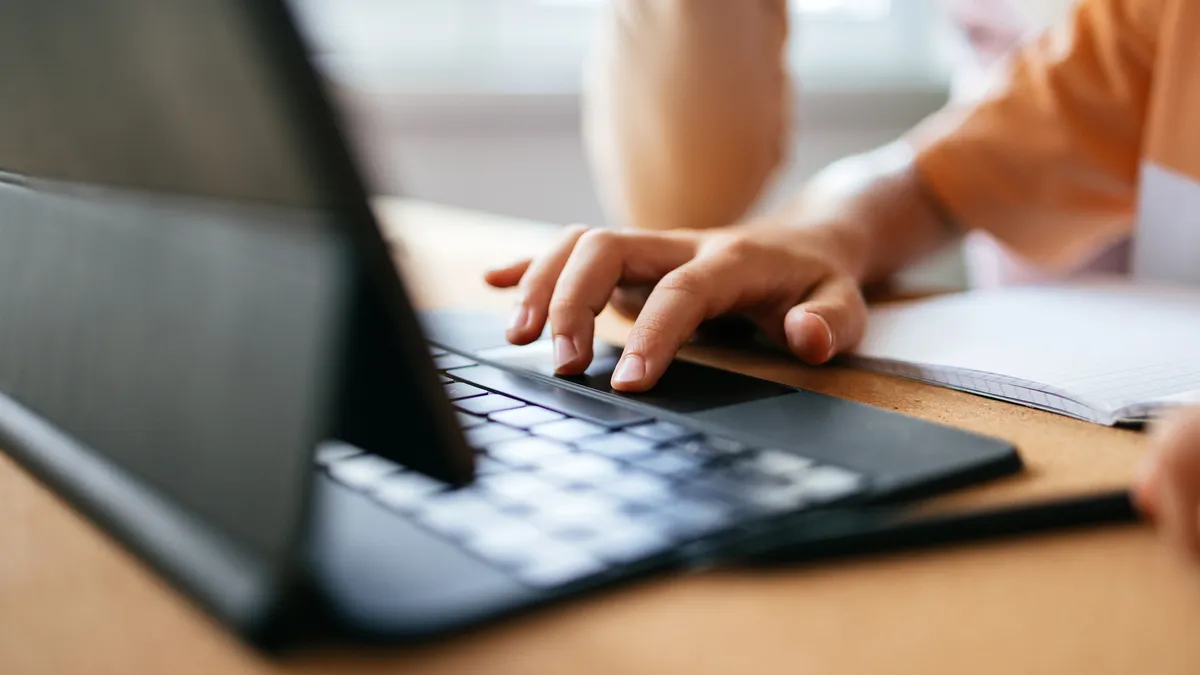 A zoomed in image of a young student's hand using a laptop computer.