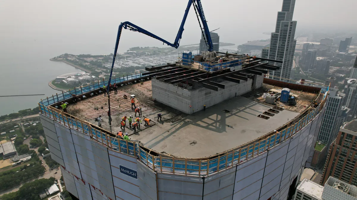 In a hazy time of day, workers bustle about on an under-construction building at the top.