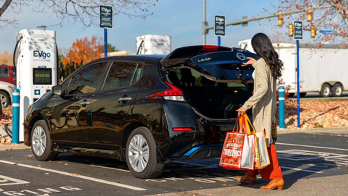 A photo of a person walking to a car at an EVgo charger with shopping bags.