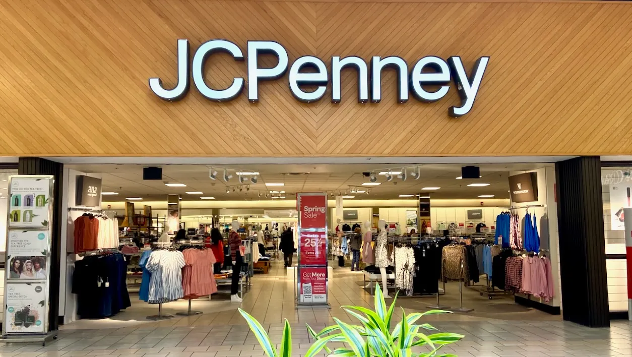 The interior entrance to a JC Penney mall store, with fronds of a plant in the foreground.