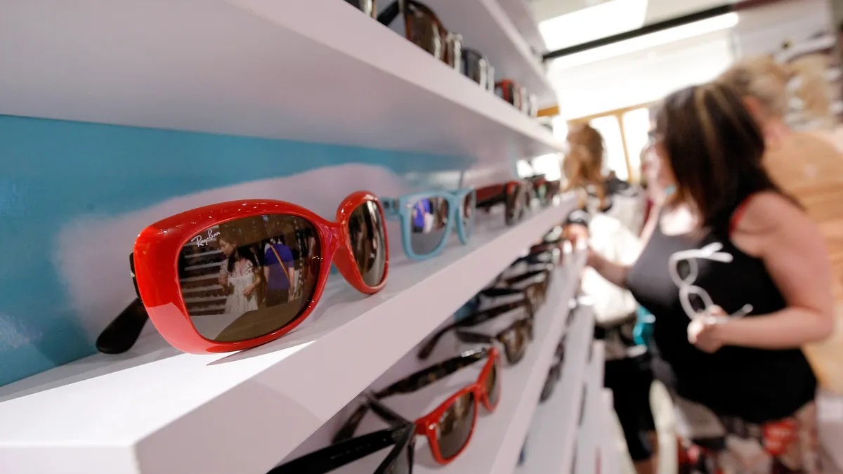 Close up of sunglasses on a store display. Shoppers browse.