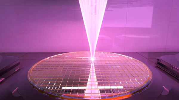 A bright beam of light etching a large round wafer, color-graded in orchid.