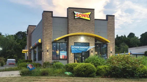 A photogrpah of a beige brick building with a yellow sign with red words that says sonic.
