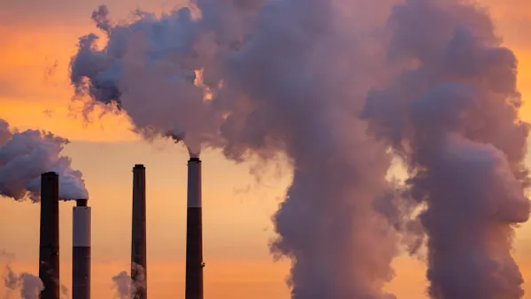 Smoke and steam pouring from smokestacks with orange sky in background.
