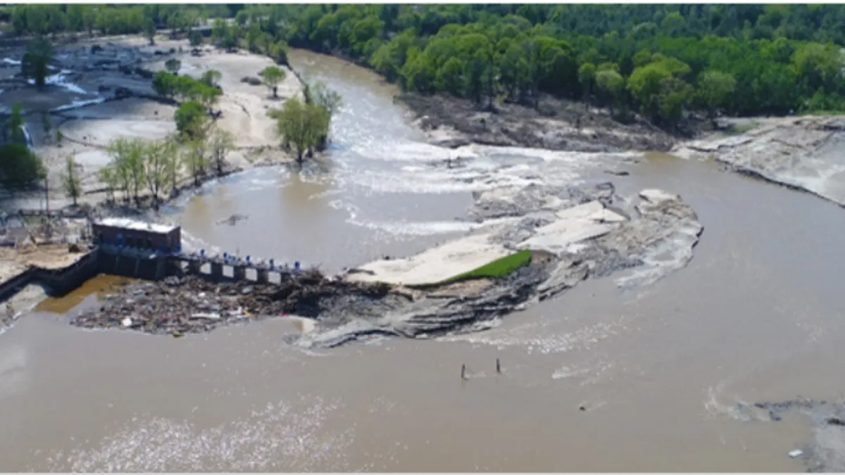 A body of water mostly submerges a broken dam structure, which stands at the mouth of a river.