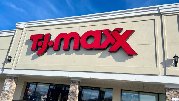 A storefront is seen at an angle, with "T.J. Maxx" in bright red letters, against a blue sky streaked with light clouds.