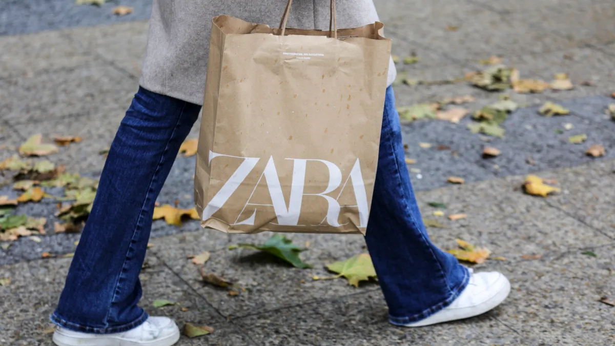 A person carries a Zara shopping bag outdoors.