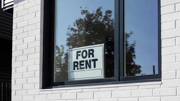 A "for rent" sign is posted behind a window of a building.