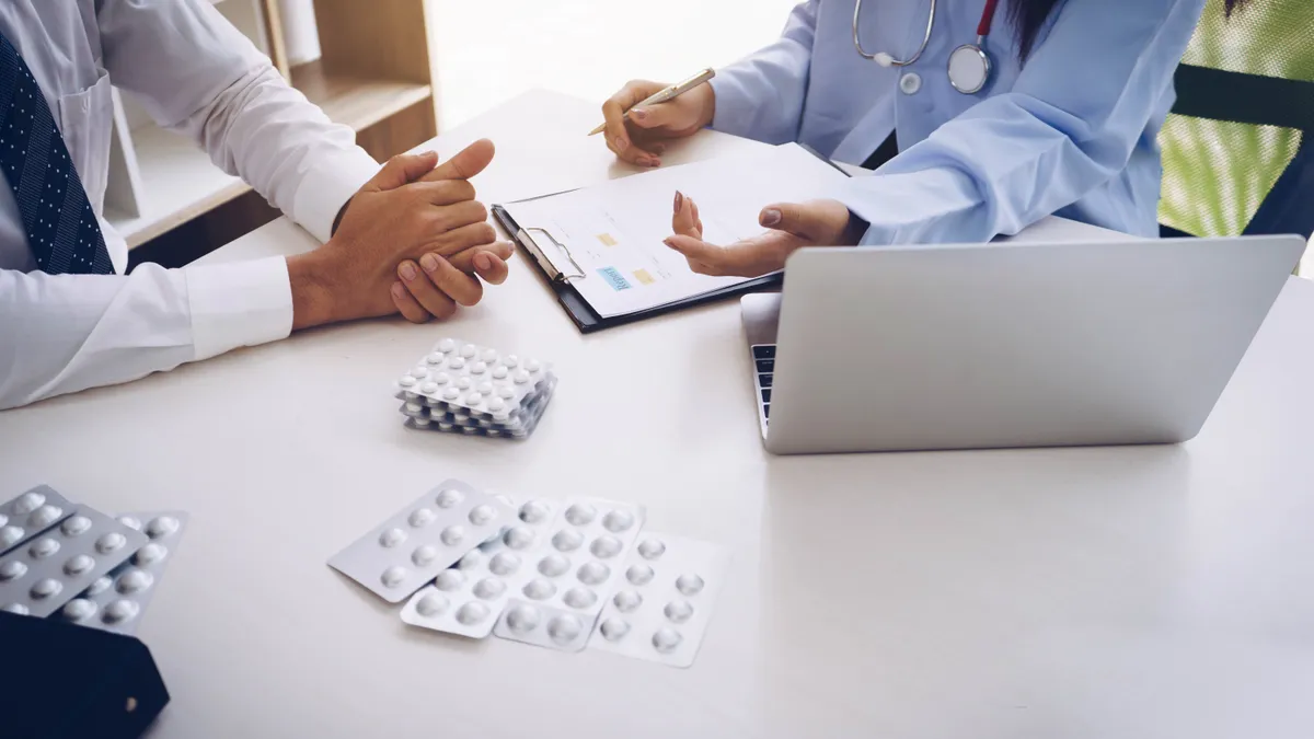 A doctor holding tablets of medicine explains options to a patient in a hospital room.