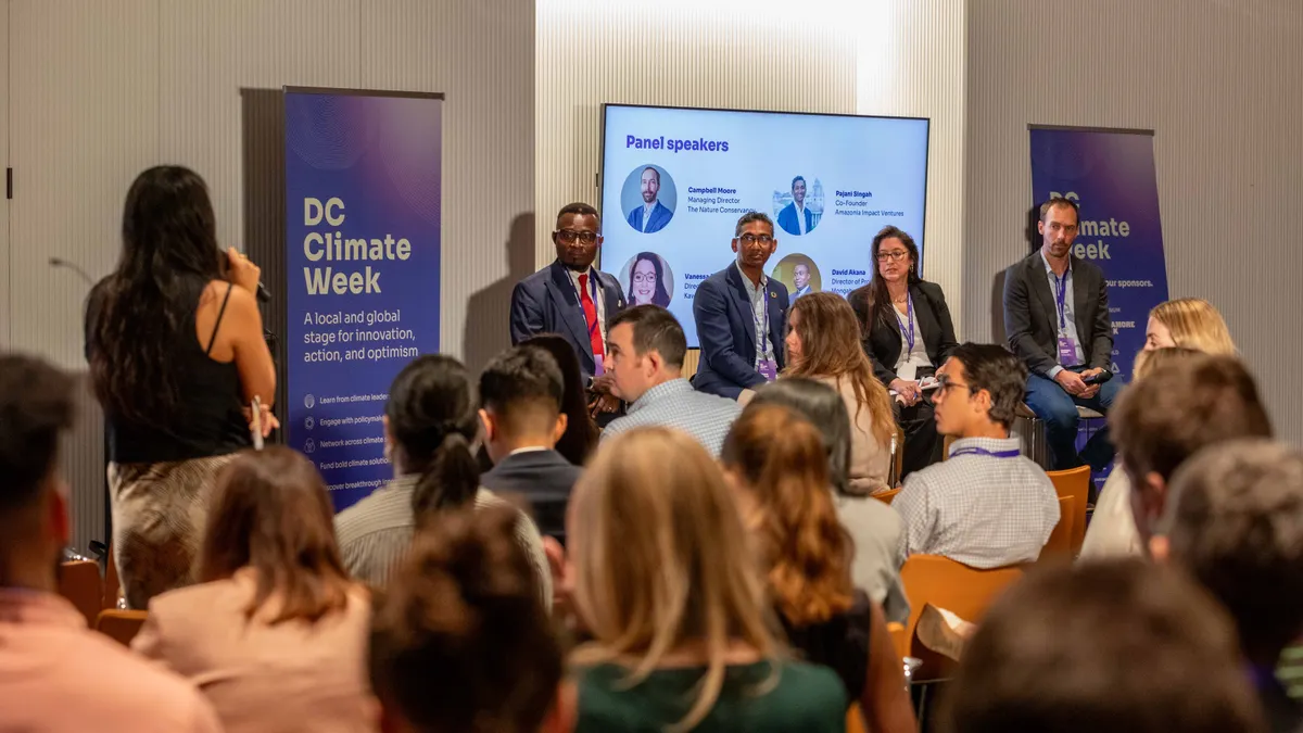 A panel of four speakers looks at a woman asking a question at DC Climate Week
