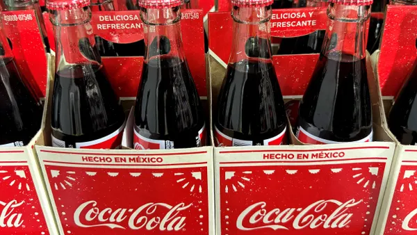 Bottles of Coca-Cola with Spanish words written on them are displayed on a store shelf.