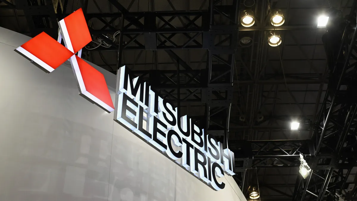 A lit black and red Mitsubishi Electric logo on a gray wall.