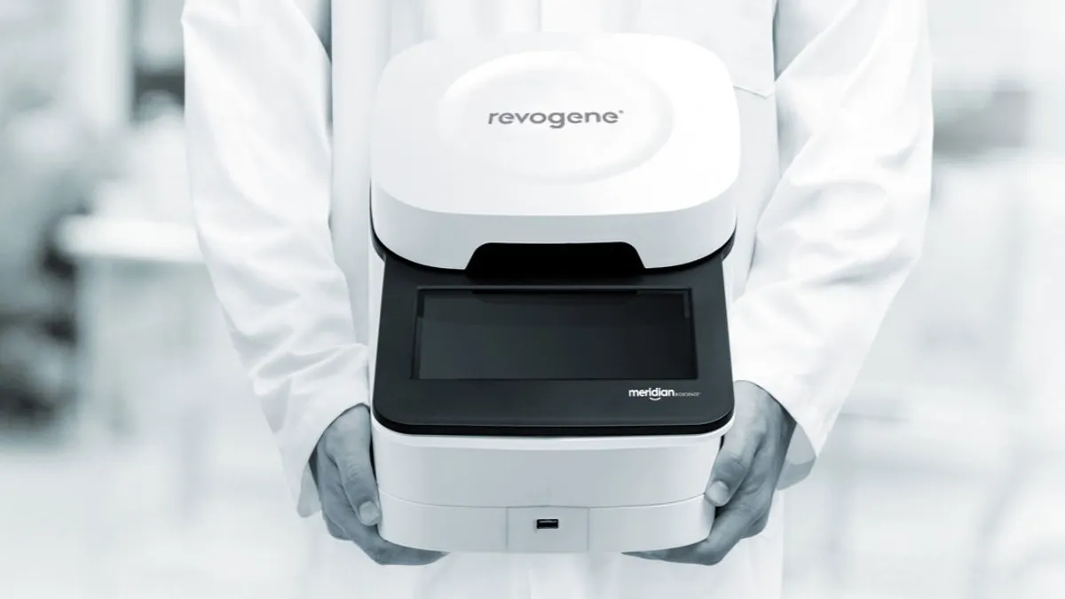 A person in a lab coat holding a Revogene Covid testing machine made by Meridien Bioscience