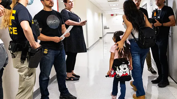 Federal officers stand across the hall from a woman and child walking down the hall of immigration court
