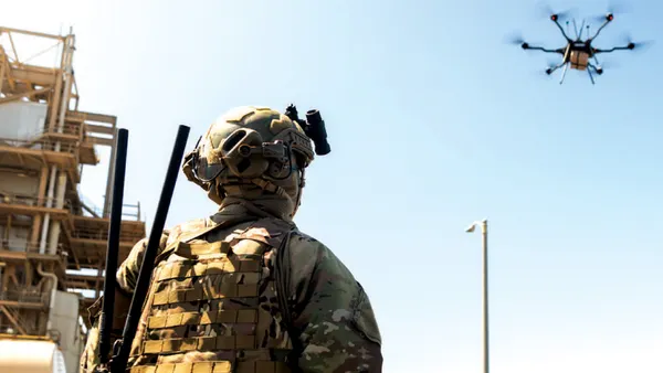 A soldier looks up at a drone in the sky.