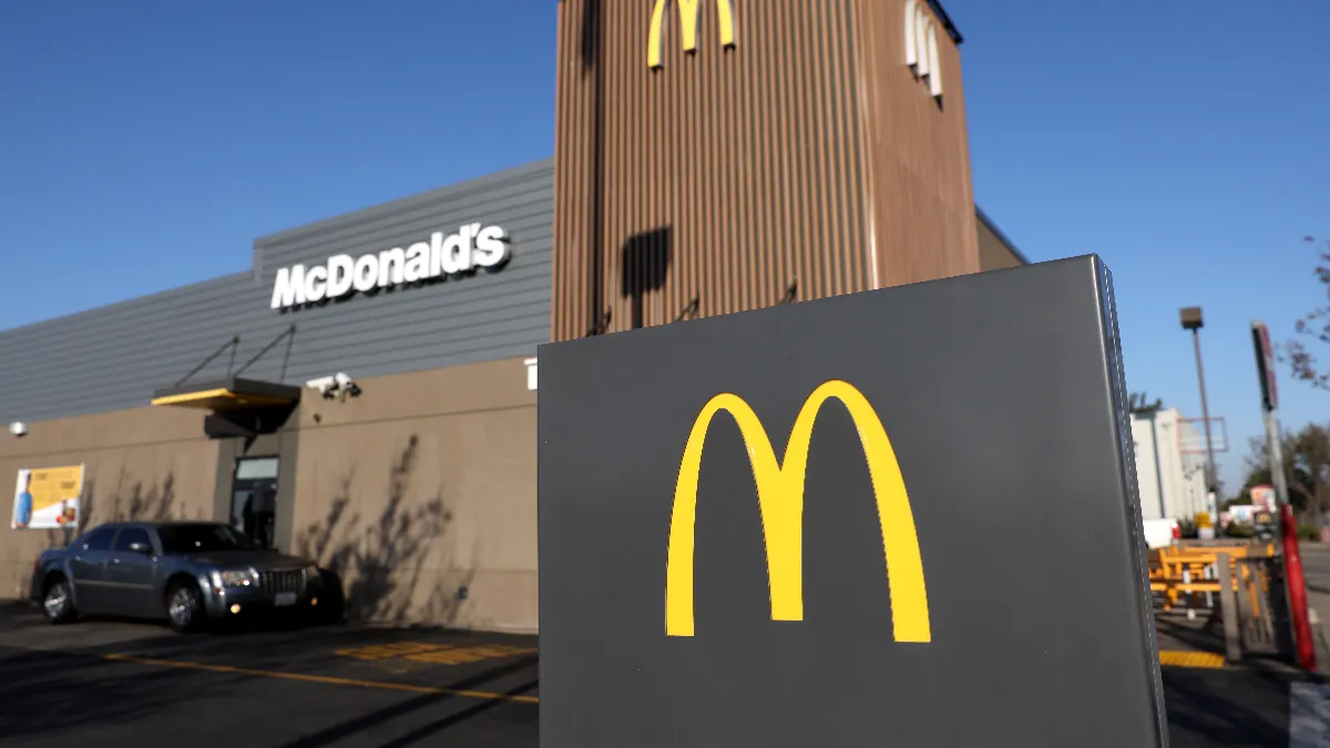 A car sits at a drive-thru at a McDonald's restaurant on a sunny day with a blue sky.