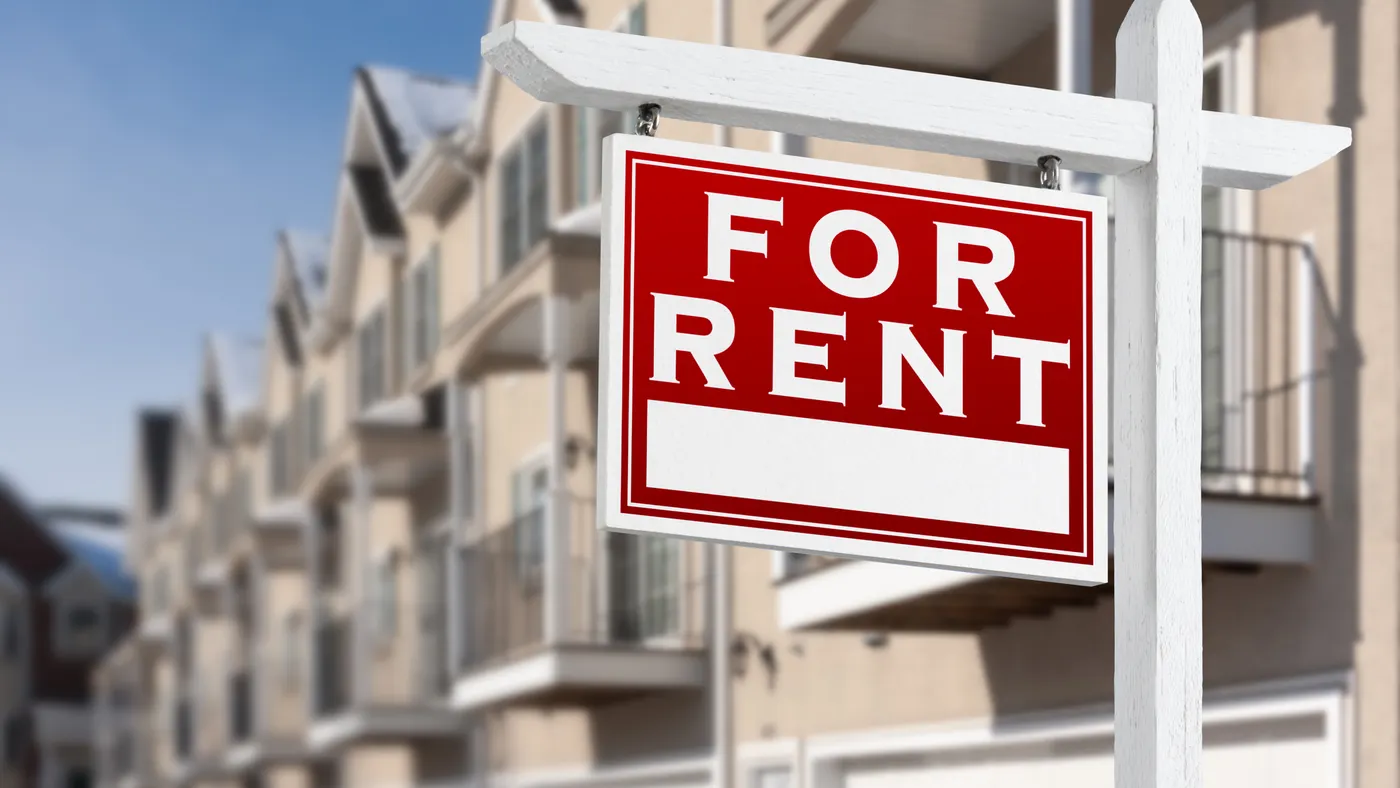 A row of homes with a red sign in the foreground that reads "FOR RENT."
