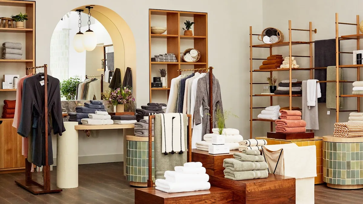 A store with bathrobes and towels displayed among green tile and wooden tables