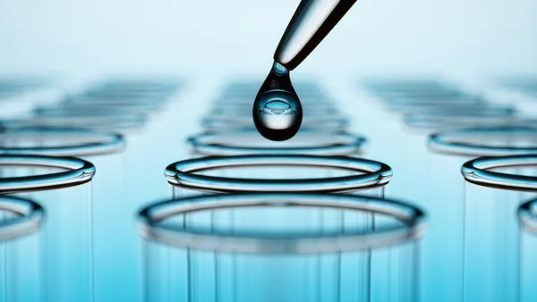 A drop of liquid is held via a pipette above a row of vials.