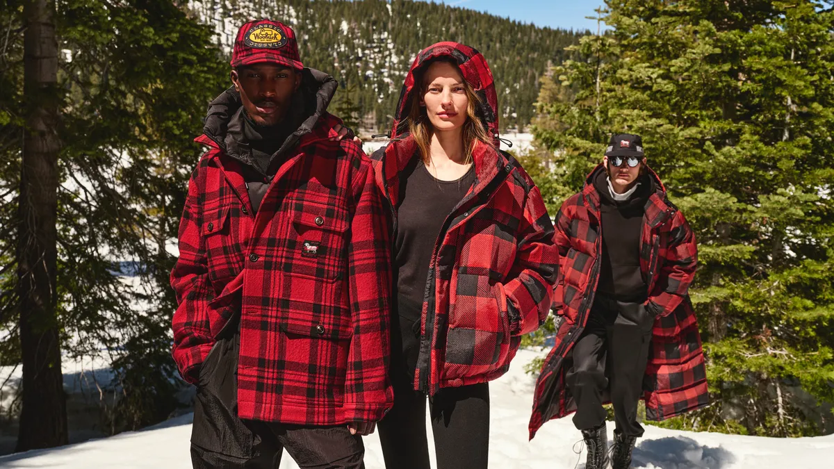 Three people in red plaid jackets stand in a snowy woods