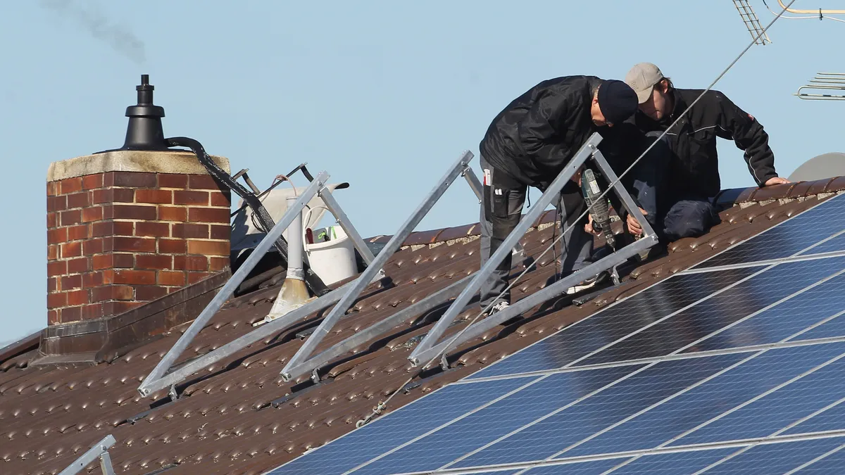 Two people install rooftop solar on a residence.