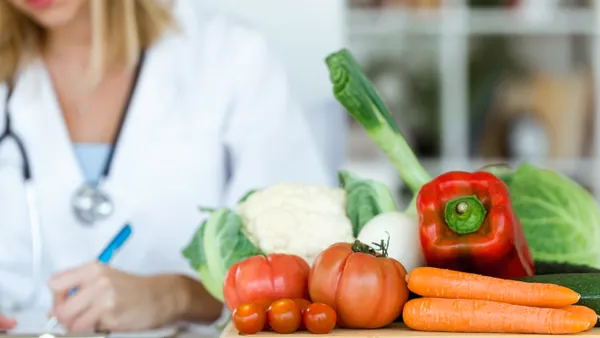 A nutritionist working at desk and writing medical records near fresh fruit.