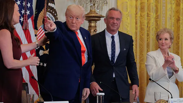 Four people are standing in a room behind a table. One person is pointing while the others are clapping.