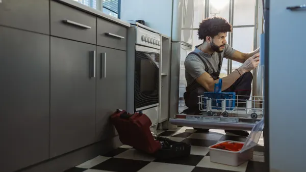 A maintenance worker repairs a kitchen appliance.
