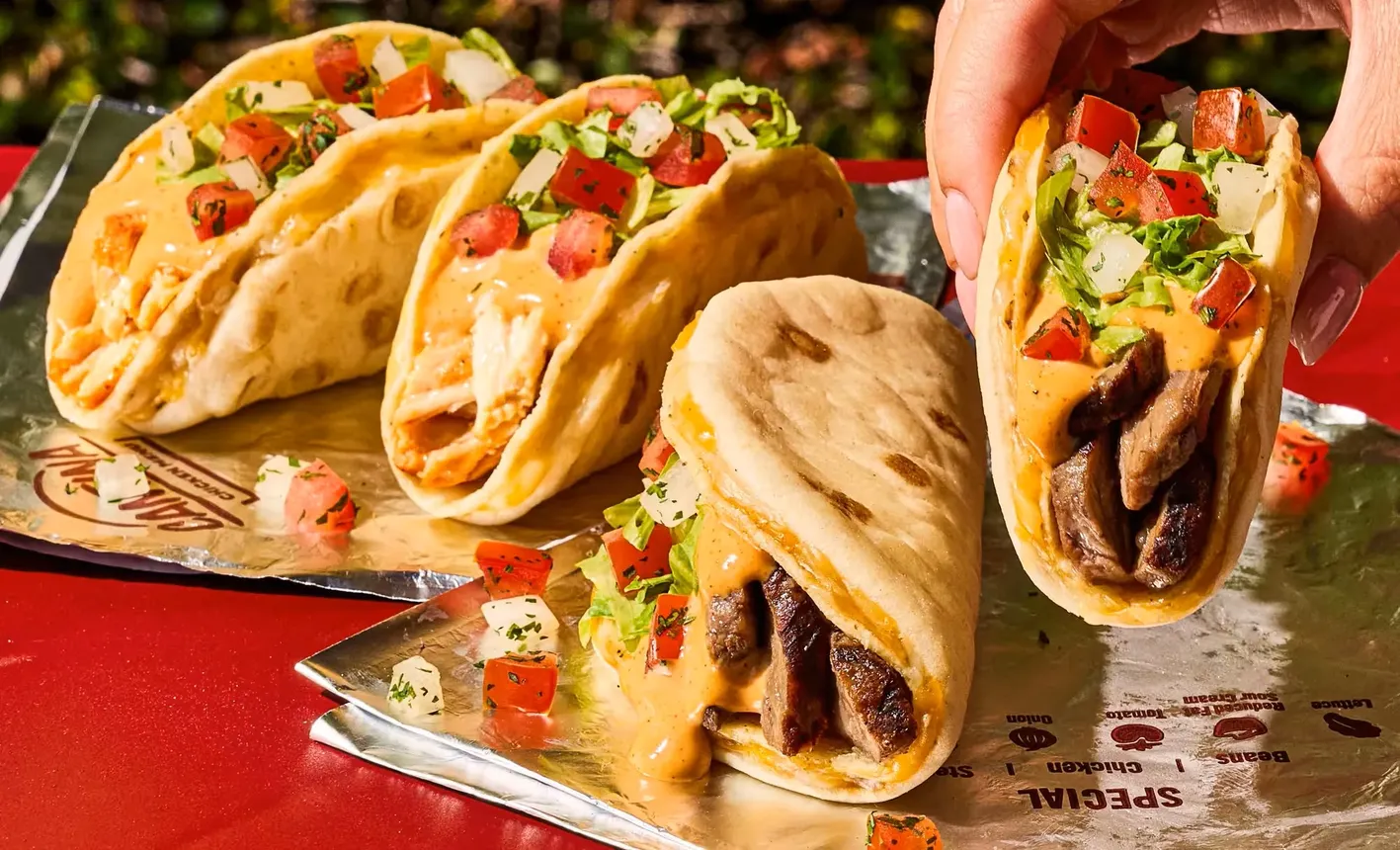 A closeup picture of a person picking up a Gordita Crunch Duo from a display of four of the Taco Bell menu items.
