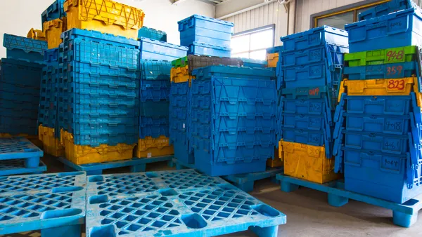 Stacks of reusable plastic transport totes sit on plastic pallets in a warehouse.