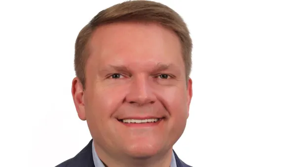 A photograph of a person wearing a suit and smiling.