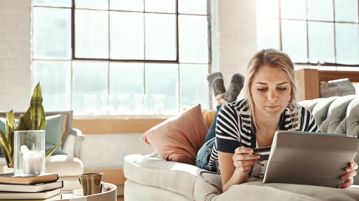 Shot of a young woman relaxing on the sofa and using a credit card with a digital tablet