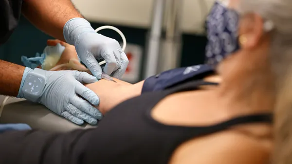 A phlebotomist inserts an intravenous line into the arm of a patient.
