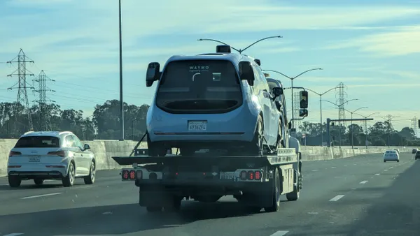 A blue vehicle on a flatbed truck along a highway with other cars.