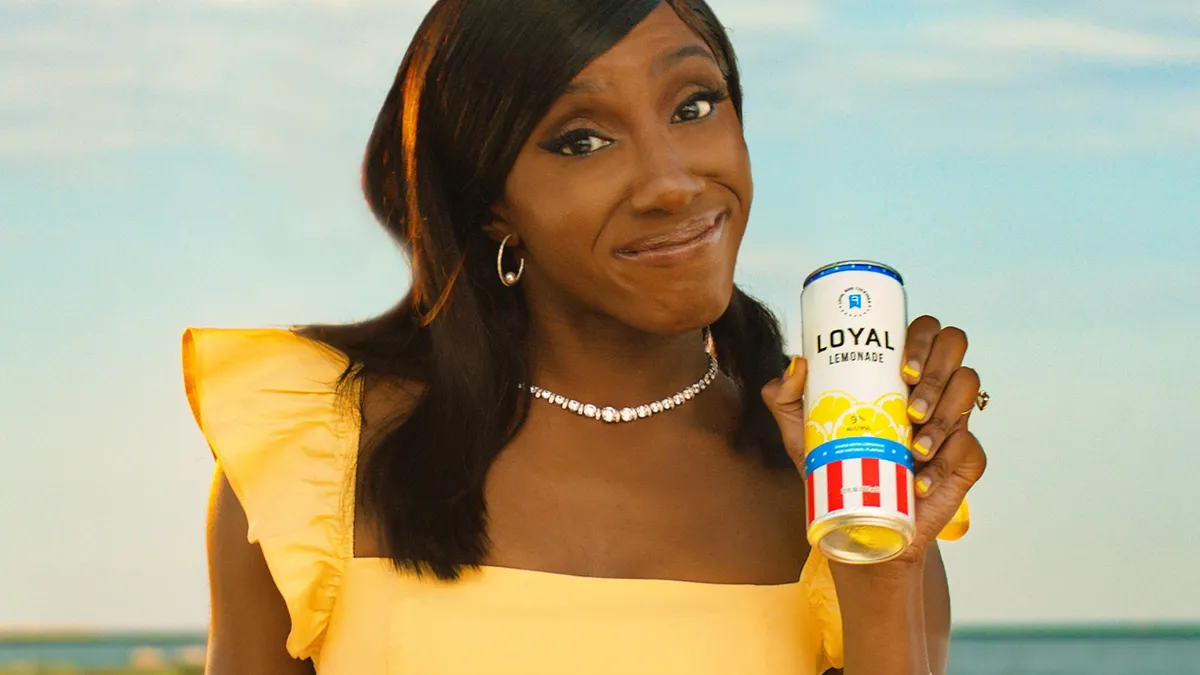 Comedian Ziwe Fumudoh holds a can of Loyal 9 wearing a yellow dress.