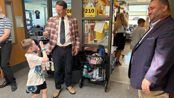 A man superintendent in a plaid jacket greets an elementary student with a fistbump in a school hallway on the first day of school..