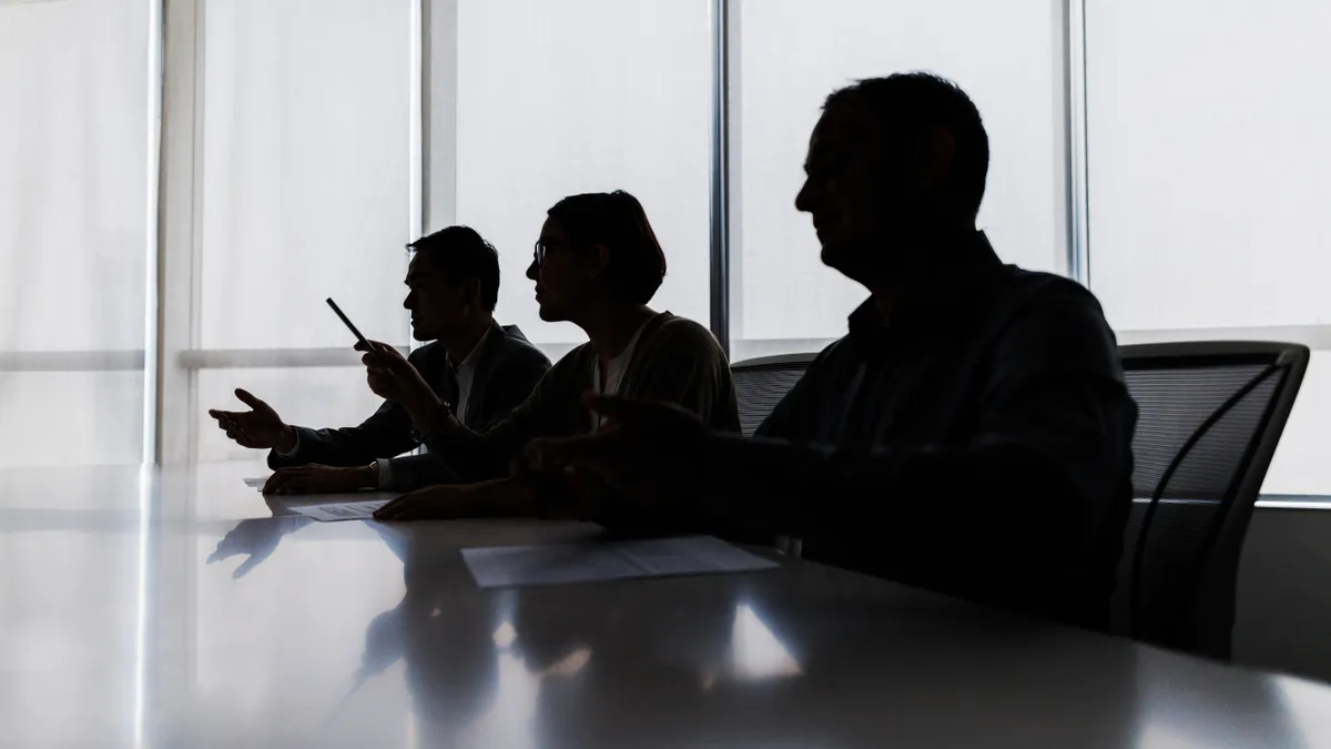 Silhouette of several business people at a conference room table.