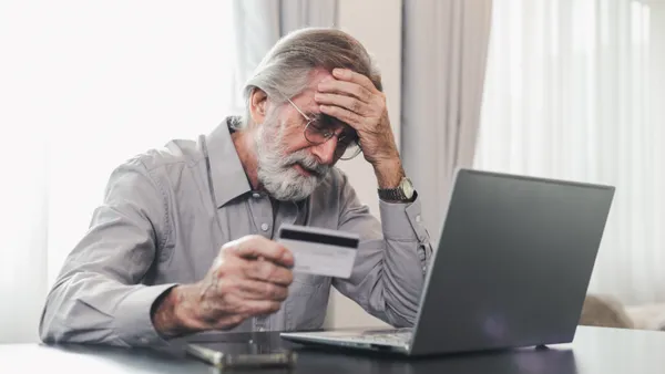 Man leans over laptop with head in hand looking at credit card.