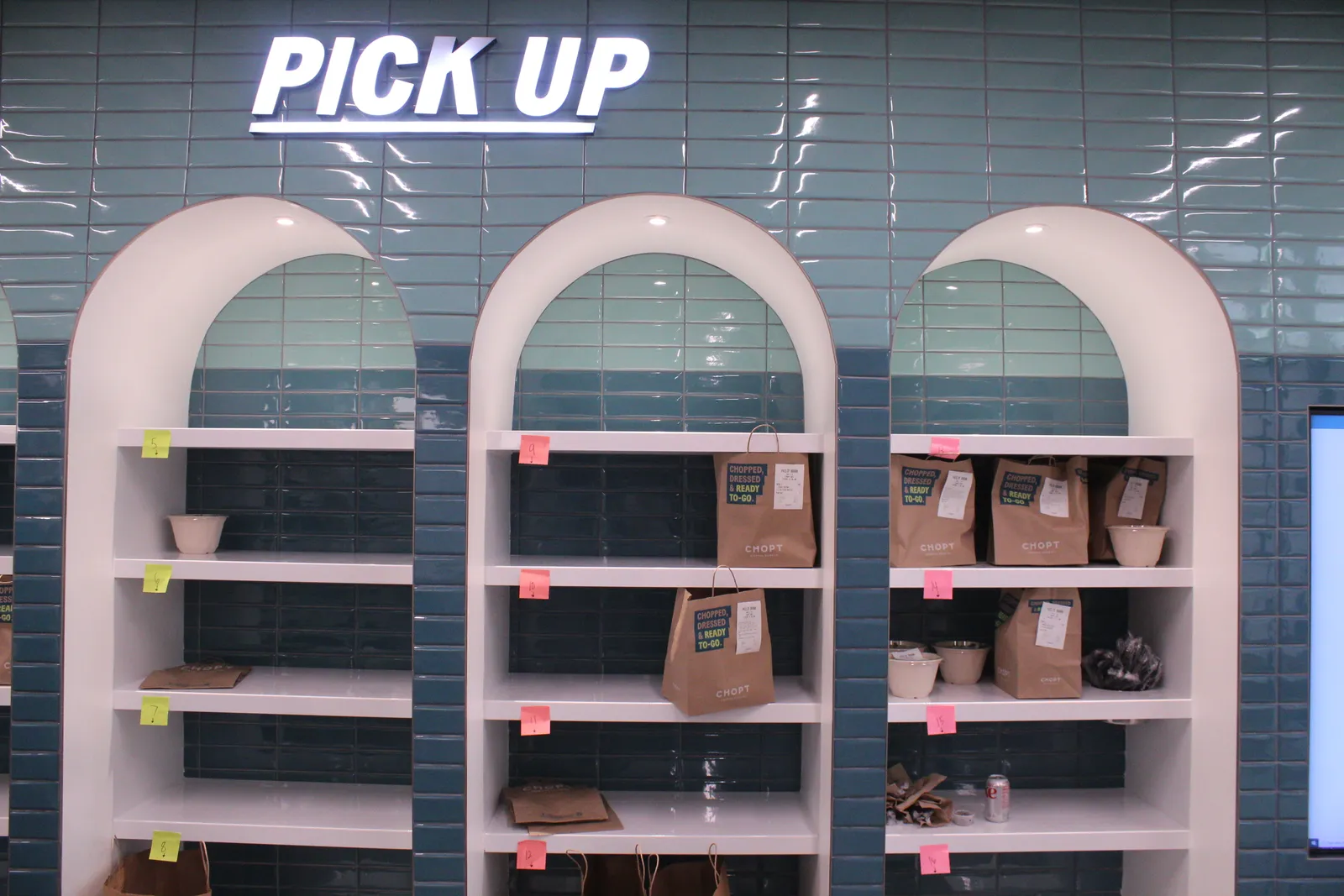 A green wall with three arches that contain white pickup shelves with bags of food.