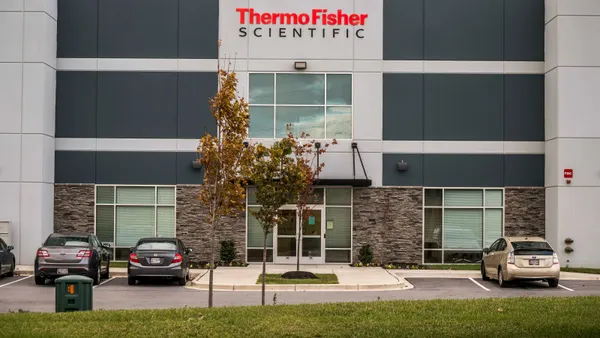 Exterior of a modern Thermo Fisher Scientific building featuring a prominent sign above a glass entrance, with cars parked in front.