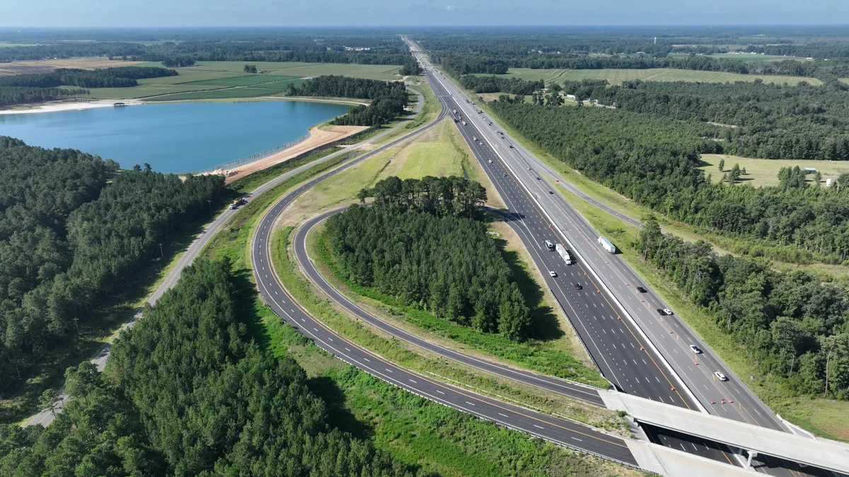 A aerial photo showing new highway roads amid a verdant and lush backdrop with some water in the background.
