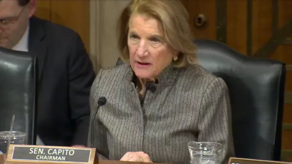 A woman speaks from a dias with a name plate saying Sen. Capito.