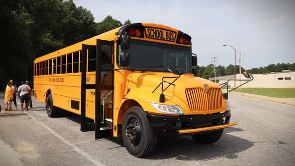 A school bus with adults near its rear door