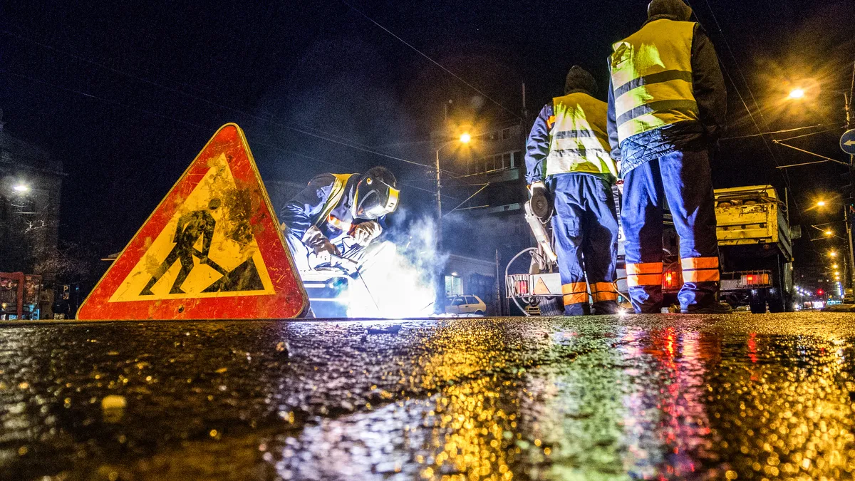 Low angle view of street workers and a welder while repairing the rail tracks in the city at night.