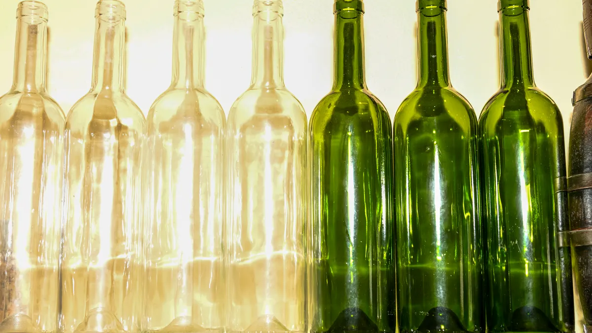 Four clear empty glass wine bottles standing next to three green empty glass wine bottles