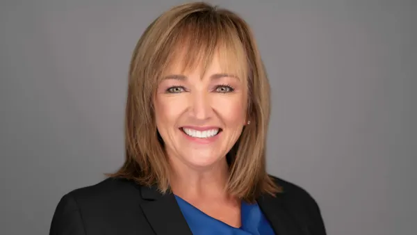 A photograph of a smiling person wearing a black suit jacket and blue shirt.