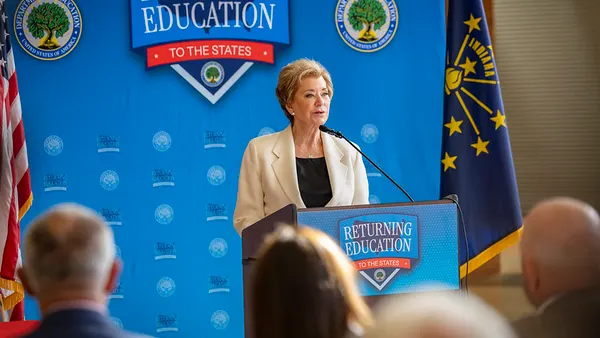 A person stands at a podium talking. Behind the person is a banner reading "Returning Education to the States"