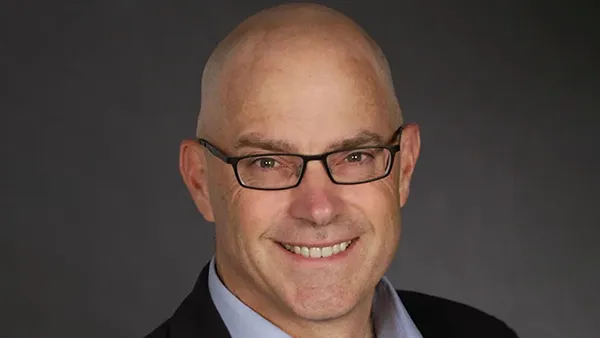 A portrait of a person smiling with glasses on a grey background.