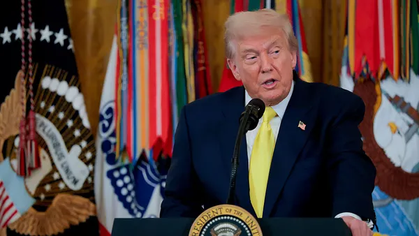 Trump speaks at a podium against a backdrop of flags.